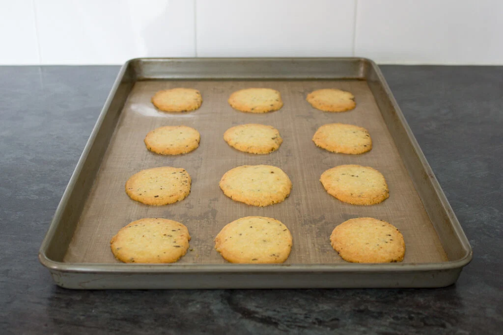 Freshly baked spicy rosemary crackers on a lined baking tray.
