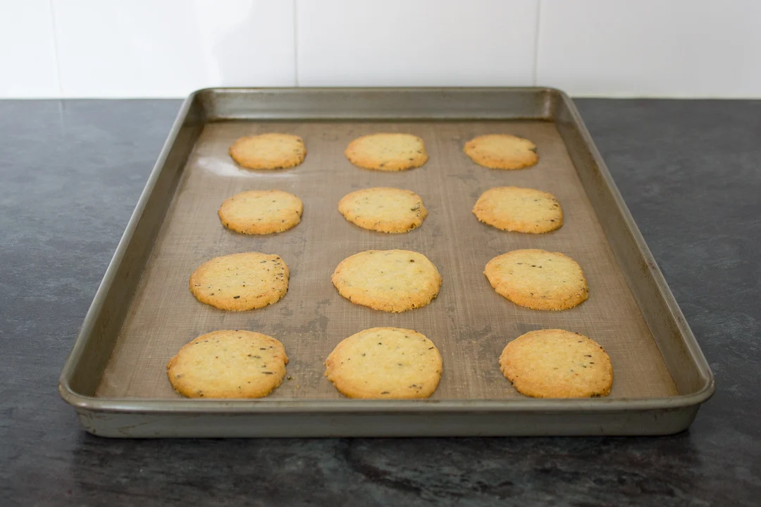 Freshly baked spicy rosemary crackers on a lined baking tray.
