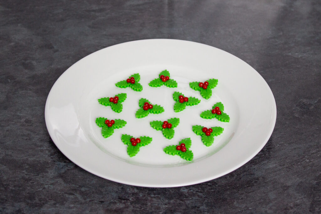 Homemade holly and ivy sugar decorations on a white plate.