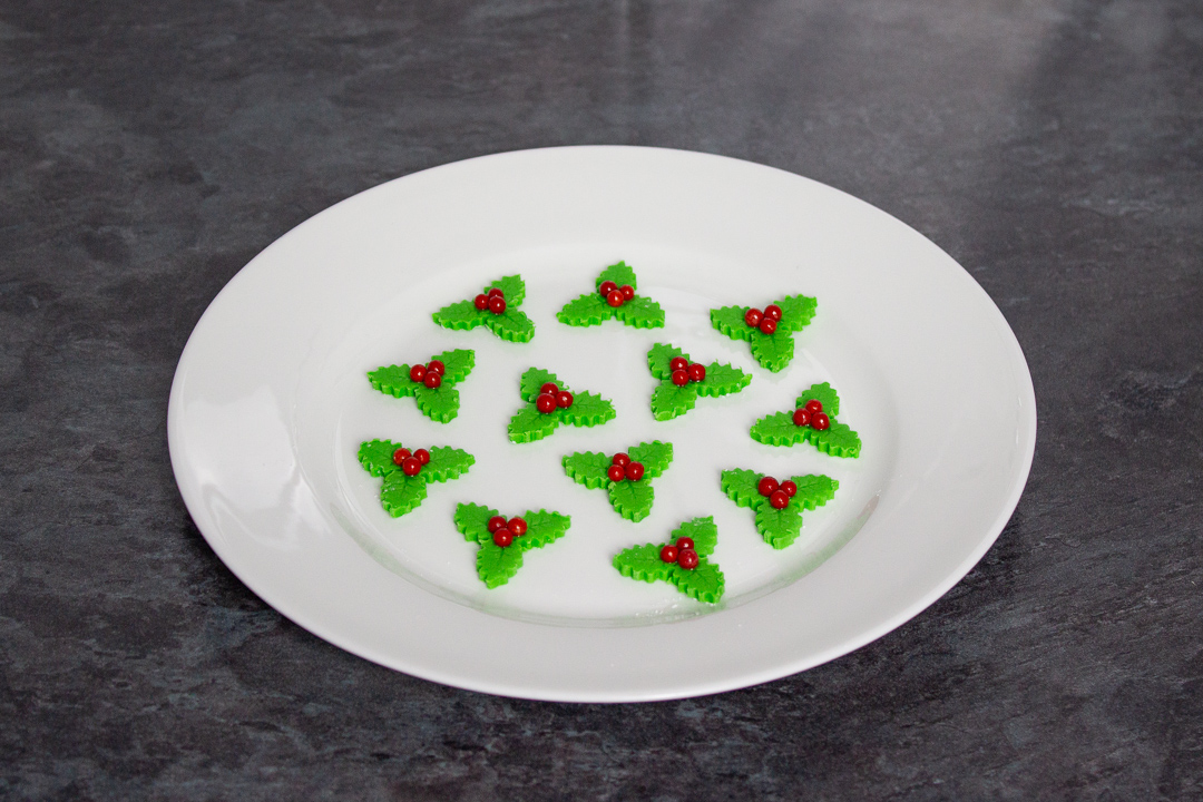 Homemade holly and ivy sugar decorations on a white plate.