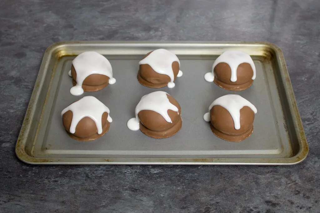 Tunnocks teacakes on a baking tray, with drizzled runny white icing over the top.