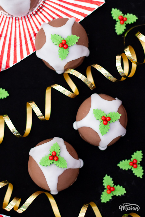 3 Tunnocks Christmas pudding teacakes on a black surface with the traditional red and silver wrapper at the side.