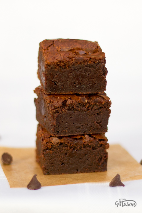 3 ultimate chocolate brownies in a stack on a sheet of baking paper.