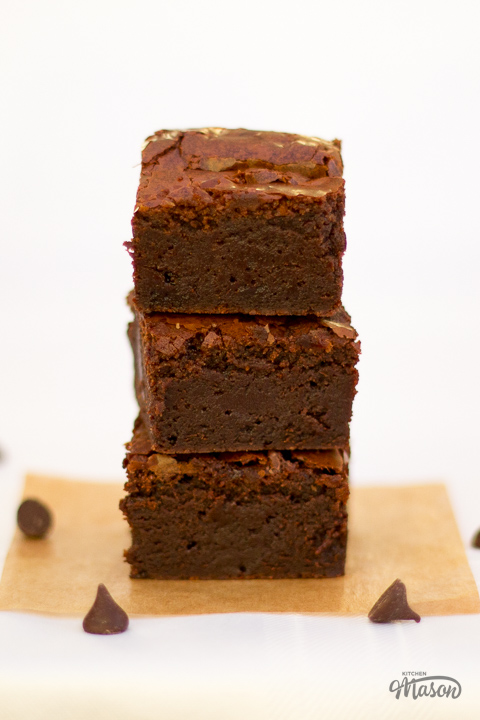 Fudgy ultimate chocolate brownies in a stack with chocolate chips scattered around.