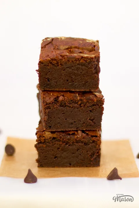 Fudgy ultimate chocolate brownies in a stack with chocolate chips scattered around.