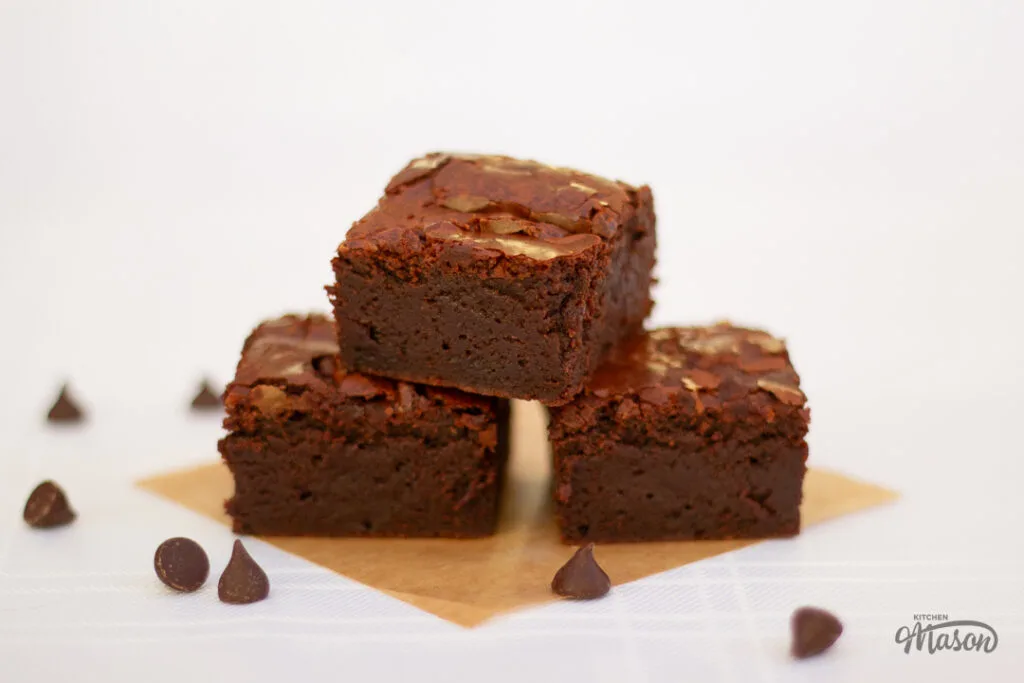 3 ultimate chocolate brownies on baking paper with chocolate chips at the side.