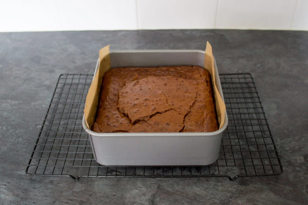 Baked chocolate brownie in a lined tin on a wire cooling rack.