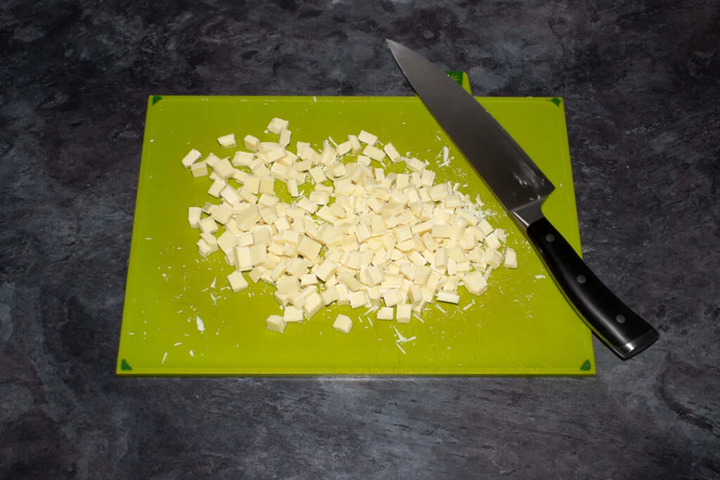 White chocolate being chopped on a green chopping board with a sharp knife.
