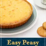 A white chocolate lemon tart on a serving plate, with a cup of tea and spare biscuits to the side. A text overlay says "Easy peasy white chocolate lemon tart".