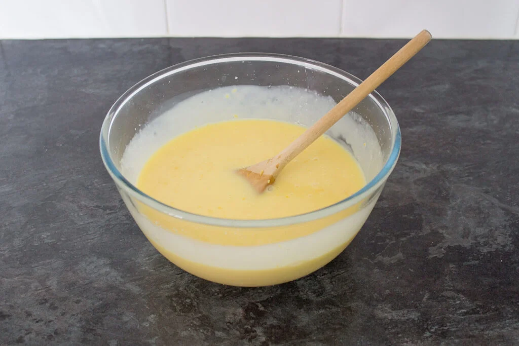 The lemon white chocolate ganache filling in a large mixing bowl with a wooden spoon.