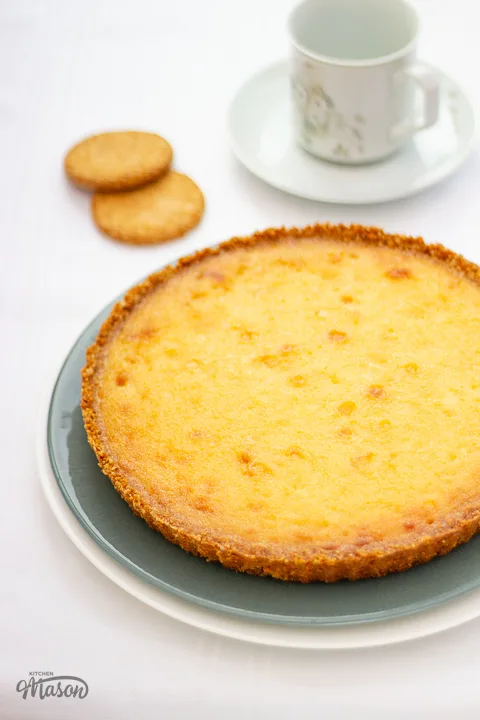 A golden white chocolate lemon tart on a green serving plate with spare oat biscuits to the side.