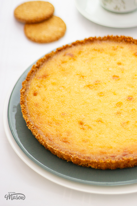 A close up of a whole white chocolate lemon tart on a green serving plate.