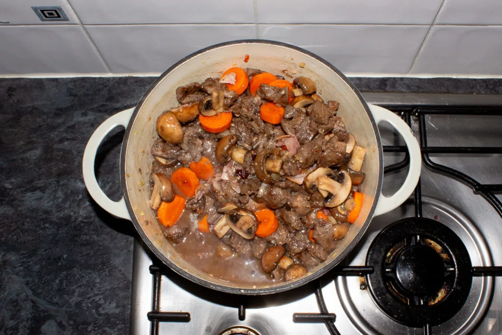 Beef casserole coming to the boil in a large dish on the stove top.