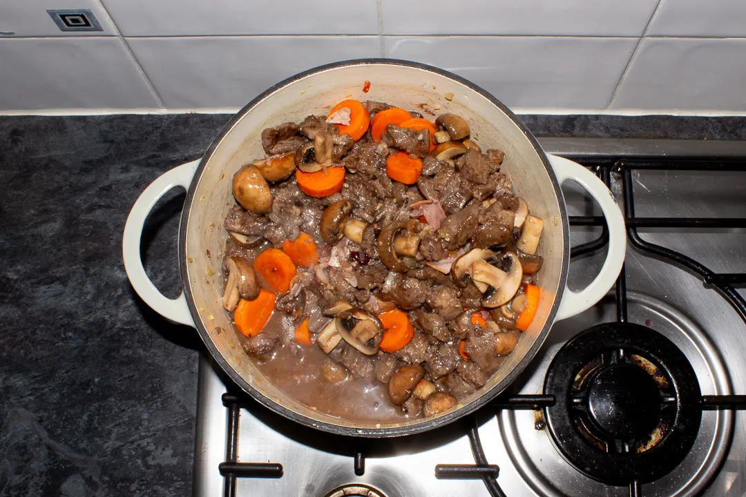 Beef casserole coming to the boil in a large dish on the stove top.