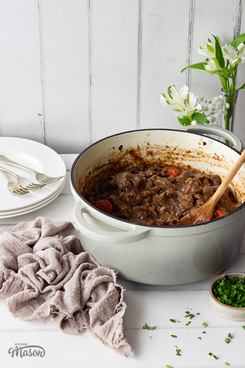 Beef casserole in a large dish with a wooden spoon.