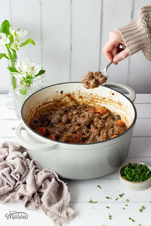 Someone spooning beef casserole out of a large pot.