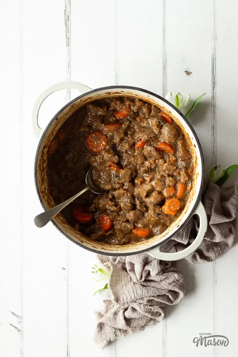Cooked beef casserole in a large pot with a big metal serving spoon in it.
