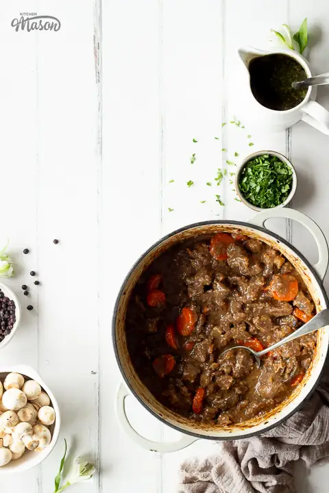 Beef casserole in a large pot, surrounded by dishes filled with ingredients.