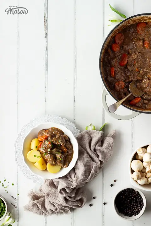 A bowl of beef casserole and boiled potatoes, with bowls of ingredients to the side.