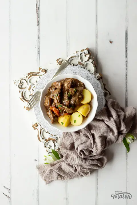 A white bowl filled with boiled potatoes and beef casserole, with a linen napkin to the side.