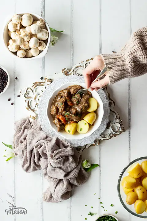 Someone forking a bowl of beef casserole and boiled potatoes.