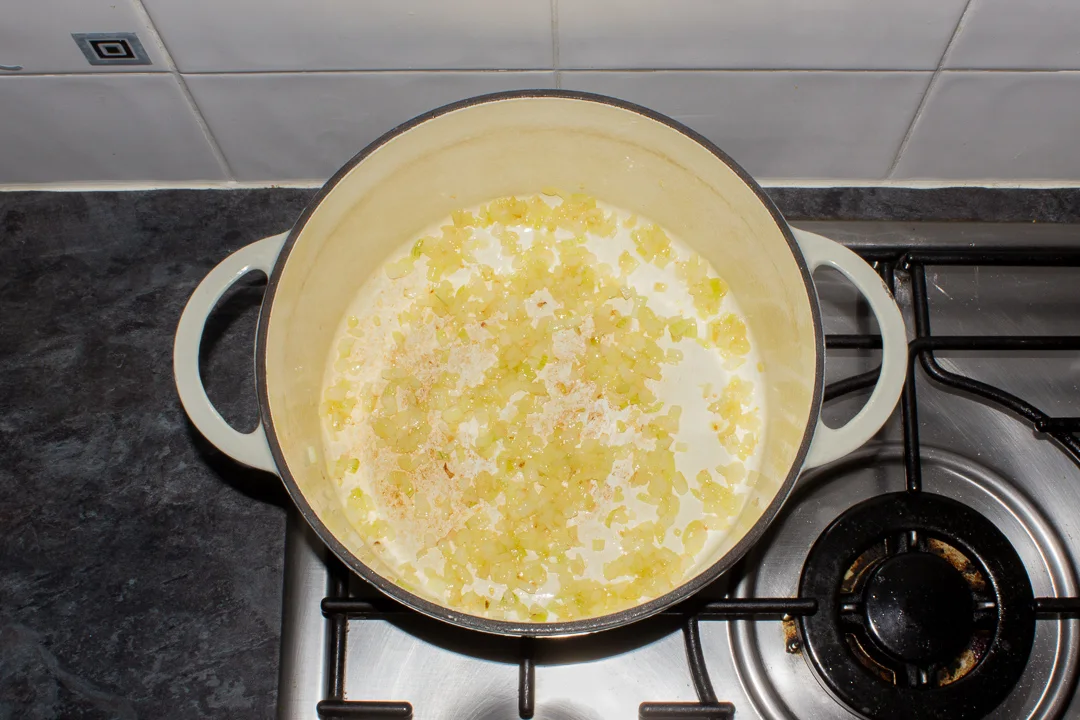 Softened onion in a large casserole dish on the stove top.