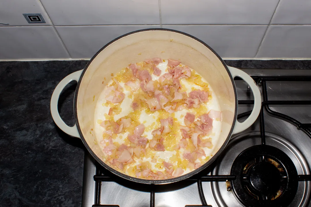 Bacon and softened onion in a casserole dish on the stove top.