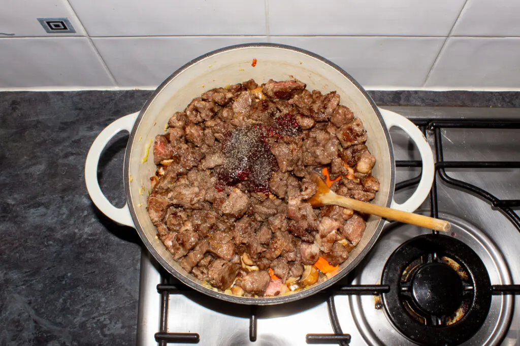 Beef casserole ingredients in a large casserole dish on the stove top.