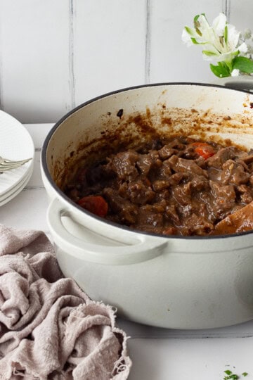 Beef casserole in a large pot with a wooden spoon.