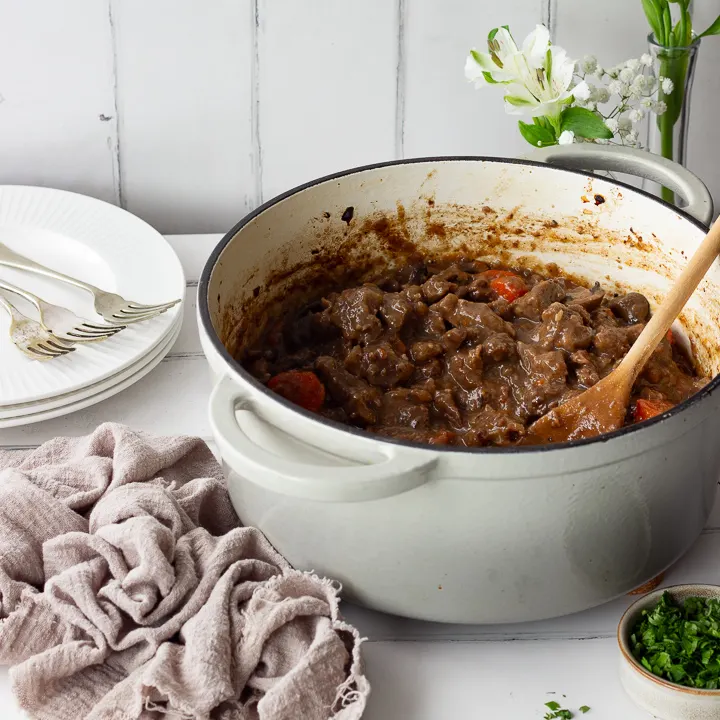 Beef casserole in a large pot with a wooden spoon.