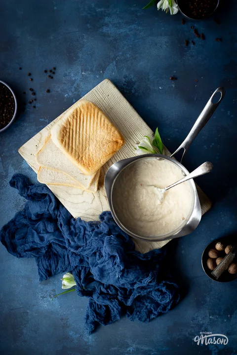 A saucepan filled with bread sauce on a chopping board, with 3 slices of bread at the side.