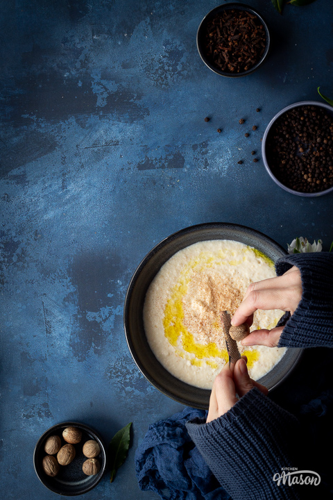 Someone grating nutmeg over a bowl of bread sauce.