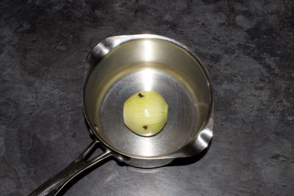 An onion studded with cloves in a saucepan.