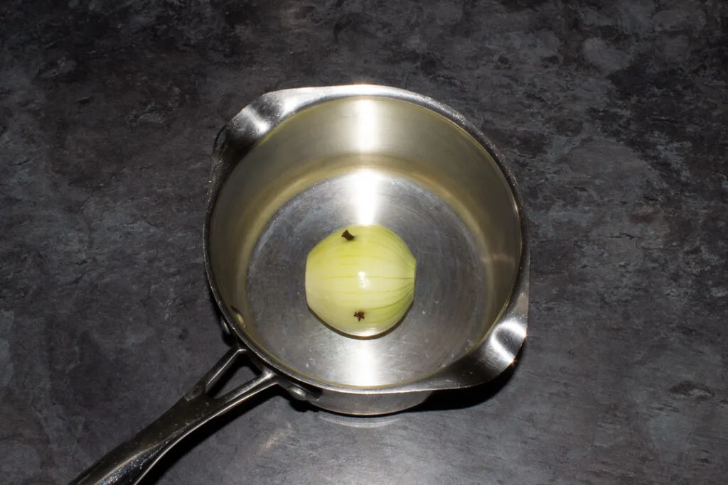 An onion studded with cloves in a saucepan.