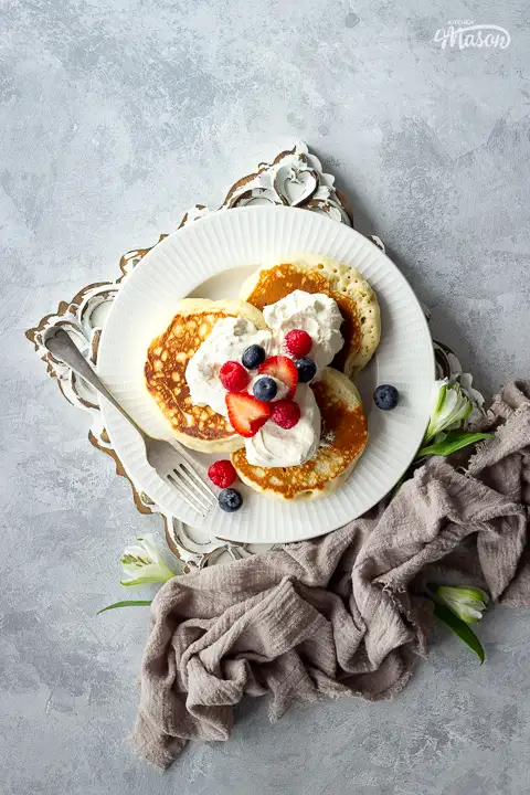 A white plate of scotch pancakes topped with cream and berries.
