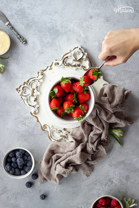 Someone spooning strawberries out of a bowl.