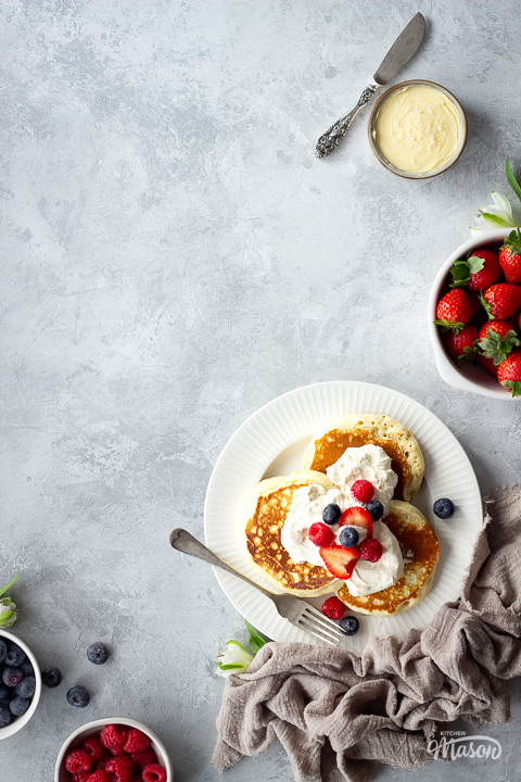 A plate of Scotch pancakes surrounded by bowls of berries and toppings.