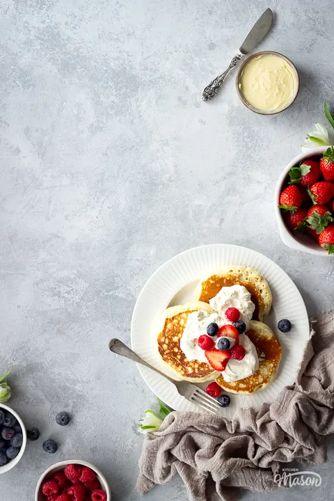 A plate of Scotch pancakes surrounded by bowls of berries and toppings.