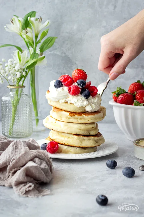 Someone forking a stack of Scottish pancakes with berries.