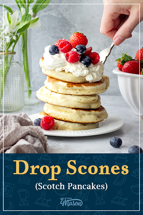 A stack of drop scones topped with berries and cream. A text overlay says "drop scones (Scotch pancakes)".