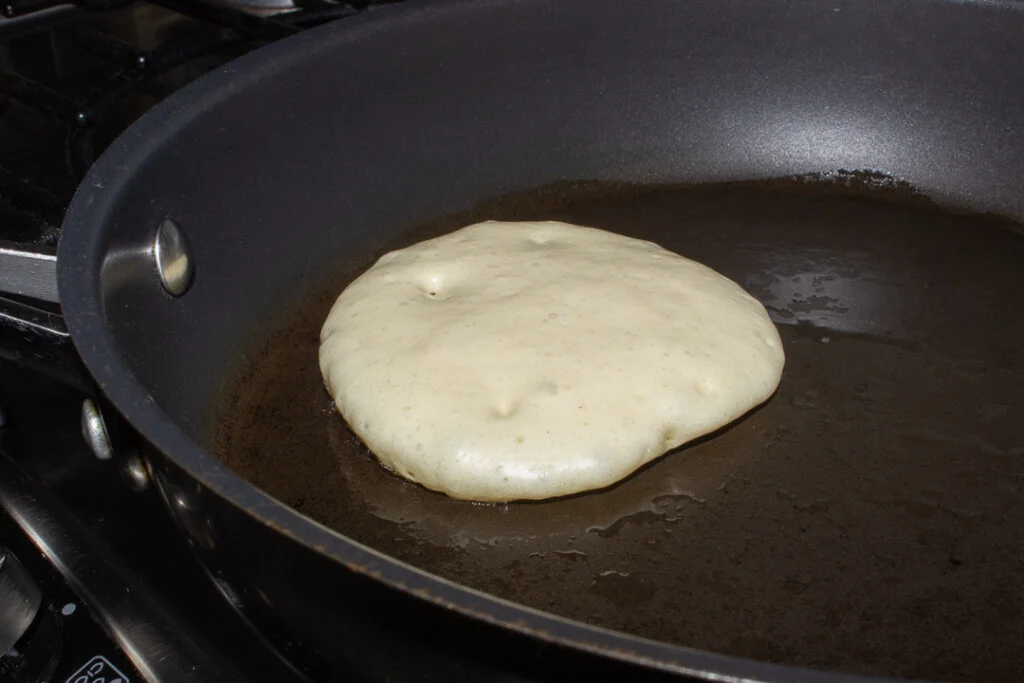 Part cooked drop scone in a frying pan.
