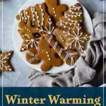 Decorated shaped gingerbread biscuits on a white plate. A text overlay says "Winter warming gingerbread biscuits".