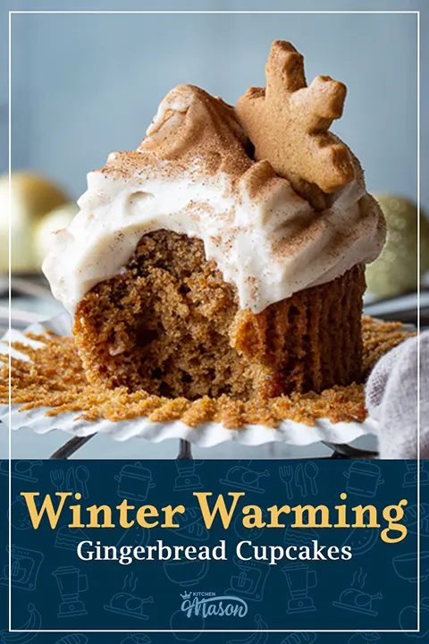A bitten into gingerbread cupcake on a wrapper, topped with a gingerbread biscuit snowflake. A text overlay says "Winter warming gingerbread cupcakes".