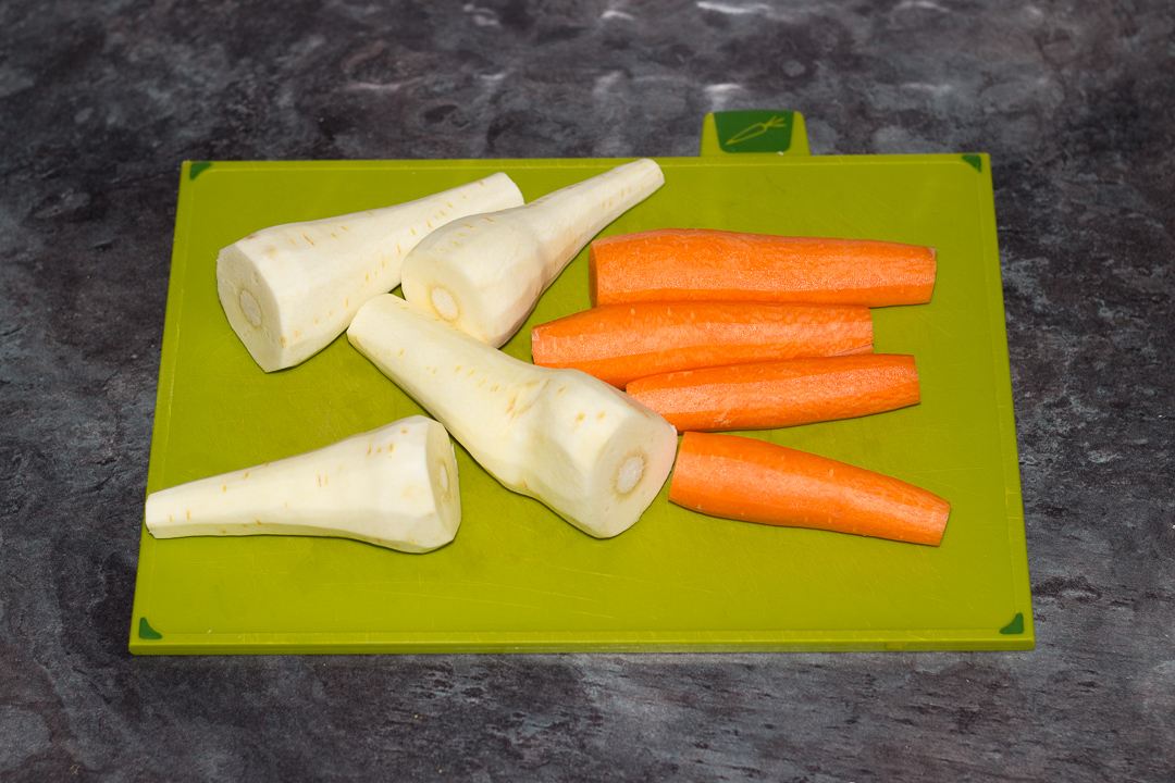 Peeled parsnips and carrots on a chopping board.