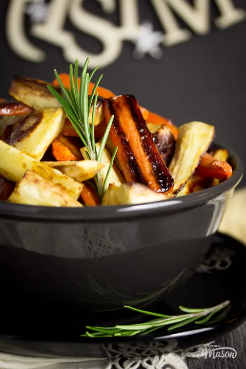 A bowl of roast parsnips and carrots on a black plate.