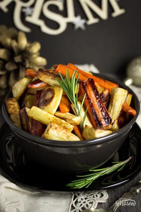 A black bowl with lots of honey roast parsnips and carrots inside, set over a beige napkin.