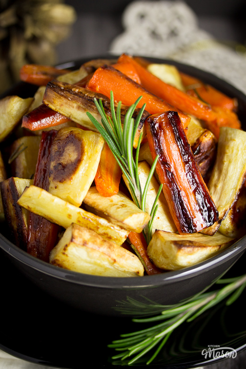 Glistening honey roast carrots and parsnips in a bowl set over a black plate.