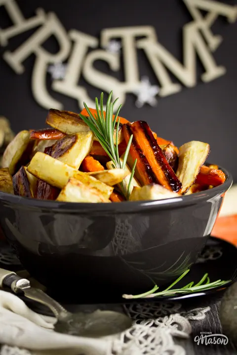 Honey roast parsnips and carrots in a black bowl topped with a rosemary sprig.