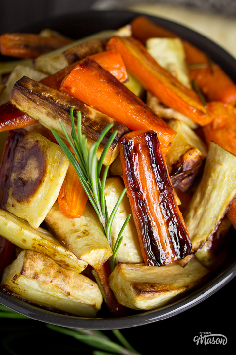 A black bowl filled with lots of honey roast carrots and parsnips.