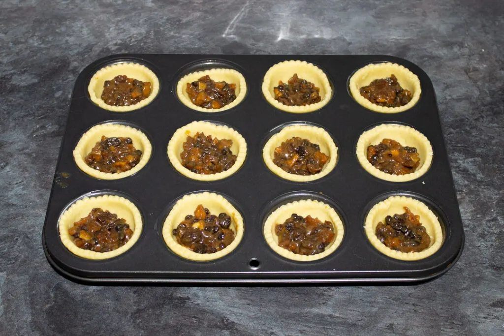 Pastry cases being filled with mincemeat in a pie tin.